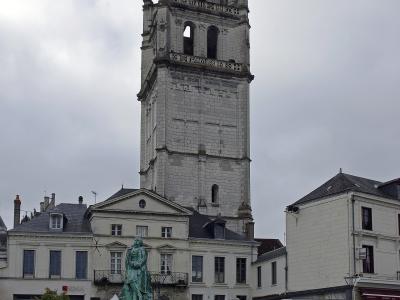 A tall, ornate stone bell tower (the Tour de l'Horloge) rises behind a statue of Alfred de Vigny in a paved town square in Loches, France.