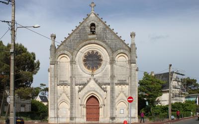 The image shows the facade of the Église Notre-Dame-des-Anges in Royan, France, a stone church with a large rose window, arched doorway, and a cross atop the gable, situated at a street corner with utility poles and a red "no entry" sign.