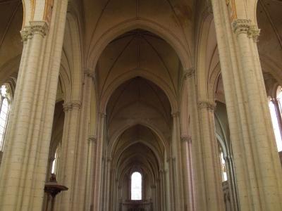 A view down the central nave of a Gothic church with rows of wooden pews.
