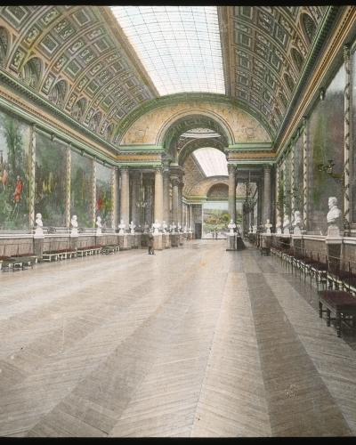 Ornate hall with glass ceiling, large murals, and marble busts.