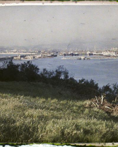 A vintage photograph showing a grassy hillside in the foreground overlooking a large harbor with a lighthouse, breakwaters, and industrial port facilities; handwritten text on the left border reads "BOUCHES-DU-RHÔNE . A 36 242".
