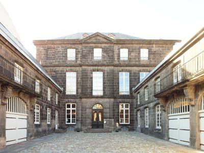 A courtyard view of a historic stone mansion with dark masonry, white-framed windows, and a central entrance, flanked by wings with white garage-style doors and iron balconies.