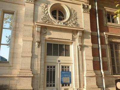 A close-up of an ornate stone entrance door with a blue sign reading "VICHY DESTINATIONS" and "PALAIS DES CONGRÈS", set into a classical-style building facade with decorative stonework, a circular window above, and adjacent brickwork.