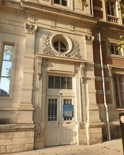 A close-up of an ornate stone entrance door with a blue sign reading "VICHY DESTINATIONS" and "PALAIS DES CONGRÈS", set into a classical-style building facade with decorative stonework, a circular window above, and adjacent brickwork.