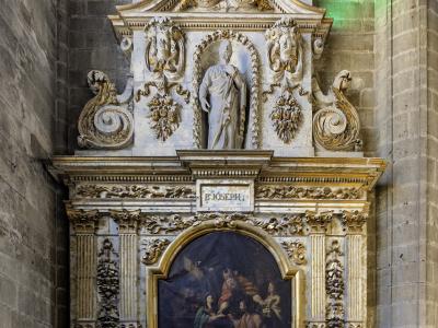 An ornate, gilded Baroque-style chapel altar featuring a statue of Saint Joseph above a religious painting, set within a stone-walled interior.
