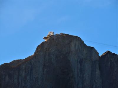 A rocky mountain summit with a cable car station structure and visible cables against a clear blue sky.