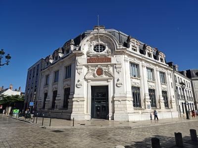 A large, ornate white stone building with "CRÉDIT LYONNAIS" signage on its facade, situated at a street corner with cobblestone pavement and pedestrians nearby.