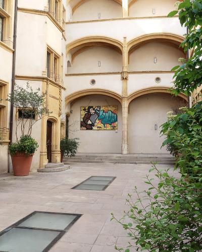 A sunlit interior courtyard of a historic stone building featuring Renaissance-style arched walkways, terracotta planters with greenery, and a colorful mural on the far wall.
