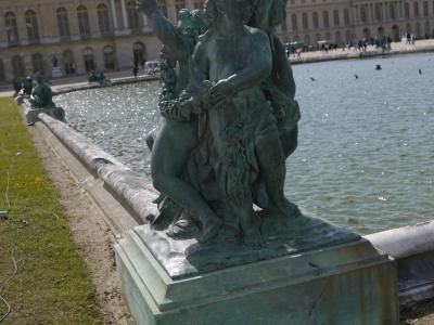 A bronze sculpture of children at a fountain in front of the Palace of Versailles.