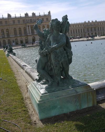 A bronze sculpture of children at a fountain in front of the Palace of Versailles.