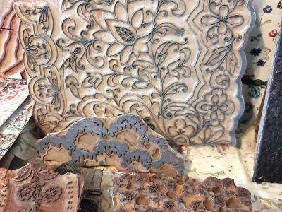 A close-up view of several large, intricately carved wooden printing blocks used for textile printing, displayed alongside printed fabric samples.