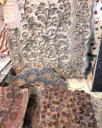 A close-up view of several large, intricately carved wooden printing blocks used for textile printing, displayed alongside printed fabric samples.