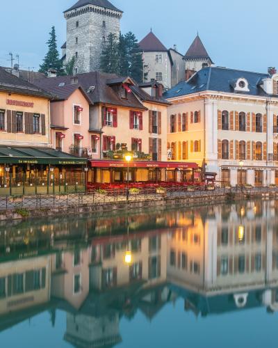 1. The image shows a canal-side view of Annecy’s old town with colorful buildings, outdoor cafes, and the Château d'Annecy (medieval castle) visible in the background, reflected in the Thiou canal.