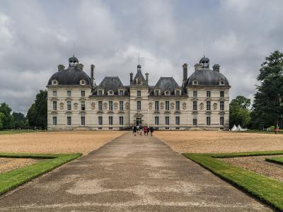 A large, symmetrical French château with a central pavilion and two prominent round towers topped with domed roofs, set behind a gravel courtyard and formal gardens under a cloudy sky.